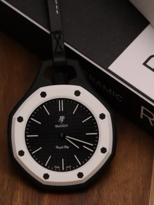 Svart och vit Swatch Royal Pop klocka - Snygg Swatch Royal Pop klocka med svart urtavla och vit ram. Klockan har en åttakantig form och tydliga indexmarkeringar. Hängs i ett svart band med vit söm. Perfekt accessoar för dig som gillar stilren och modern design.