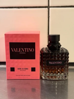 Valentino Donna Born In Roma Intense - Valentino Donna Born In Roma Intense är en lyxig parfym i en elegant, mörk glasflaska med nitar och svart lock. Förpackningen är rosa med svart text och rymmer 100 ml Eau de Parfum Intense. Flaskan har en exklusiv design som känns både modern och klassisk.
