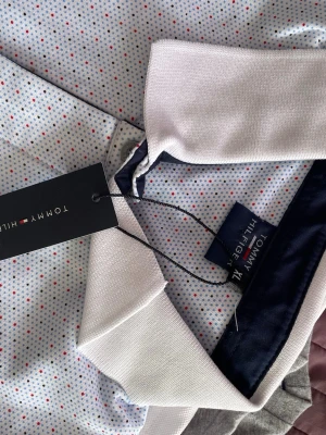 Prickig skjorta från Tommy Hilfiger - Snygg skjorta från Tommy Hilfiger i vitt tyg med små prickar i blått, svart och rött. Klassisk krage och knappstängning framtill. Perfekt för dig som vill ha en stilren men ändå lekfull look.