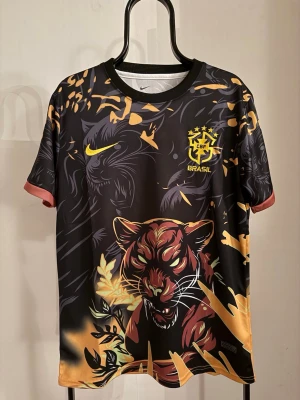 Nike Brasil t-shirt med tigertryck - Unik svart och gul Brasil t-shirt från Nike med stort tigertryck framtill och klösmärken på ryggen. T-shirten har rund hals, korta ärmar och detaljer i orange och gult. Perfekt för dig som vill sticka ut på träningen eller matchen.