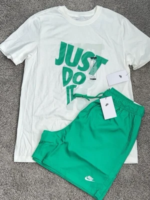 Nike sett sommar  - Snygga gröna shorts från Nike med vit logga på benet och justerbar snörning i midjan. Perfekta för sommaren och har en avslappnad passform. Materialet känns mjukt och lätt, vilket gör dem sköna att bära hela dagen.