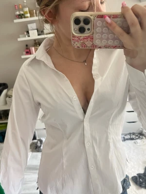 Vit klassisk skjorta från BikBok - Säljer en vit skjorta från BikBok i klassisk modell med krage och knappar framtill. Skjortan är långärmad och har en clean, tidlös look som passar till allt. Tillverkad i mjuk bomull för en bekväm känsla.