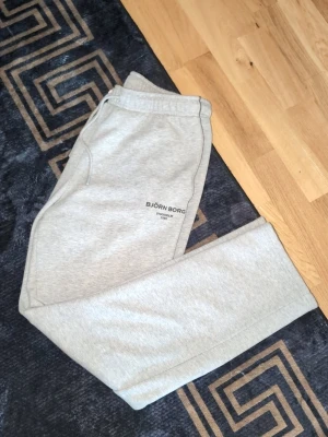 Grå mjukisbyxor från björn borg  -  Björn Borg-logga tryckt på låret. Perfekta för chill dagar eller när du vill vara bekväm. Köpta cirka 1.6 månader sen med en björn bprg (svart) t shirt  säljs som dress eller separat  ..käpa som dress kan pris komma att bli billigare max använt 3 ggr ..450 kr båda , bara tshirt värd 399, dessutom materialet är syntet väldigt skön tshirt och mjukisen också riktigt skön material ..skön sommar dress kanske ? 