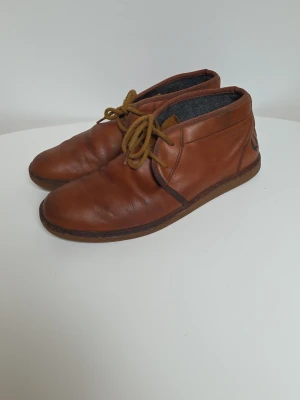 Bruna läderloafers från Fred Perry - Säljer ett par bruna loafers från Fred Perry i äkta läder. Skorna har snörning, låg profil och diskret logga på hälen. Insidan är fodrad med grått tyg och sulan är i gummi. Perfekta för en stilren och avslappnad look. Tvättade och uppfixade nydligen.