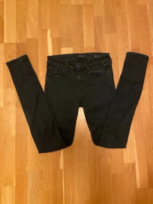 Svarta Replay jeans - Säljer ett par svarta Replay New Luz jeans i storlek 28. De har en klassisk femficksdesign, skinny fit och snygga detaljer som Replay-logga på bakfickan och blå knapp framtill. Jeansen är i stretchigt material för extra bekvämlighet.
