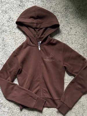 Brun hoodie med tryck och dragkedja - Säljer en brun hoodie med dragkedja och huva. På bröstet finns ett litet tryck och på ryggen ett stort motiv med texten 'Honest Soul' och 'Love' i beige. Hoodien har långa ärmar och ribbade muddar. Perfekt för en chill och avslappnad stil.