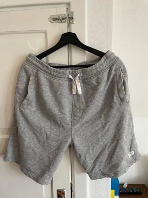 Grå mjukisshorts med snörning - Gråa mjukisshorts med snörning i midjan och två sidofickor. Perfekta för en avslappnad stil och tillverkade i mjukt bomullsmaterial. Klassisk design utan synliga loggor förutom en liten etikett nertill.