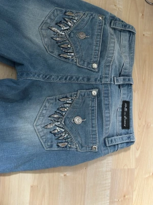 Jeans med coola fickor! - Snygga blå jeans från ”Stella in dreams” som jag köpte i USA. Med bootcut design och coola paljettdetaljer på bakfickorna. De har coola knappar över hela jeansen och är i mycket bra skick! 