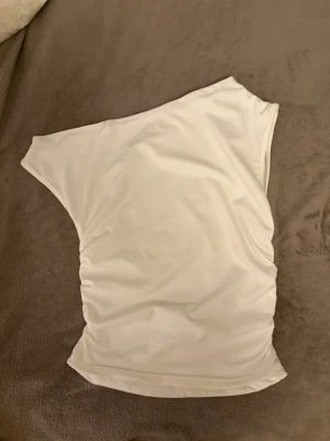 Vit oneshoulder topp - Snygg vit oneshoulder topp i mjukt material. Toppen har en clean och enkel design utan mönster eller detaljer, perfekt för dig som gillar minimalistisk stil. Passformen är normal och tyget känns stretchigt och bekvämt.