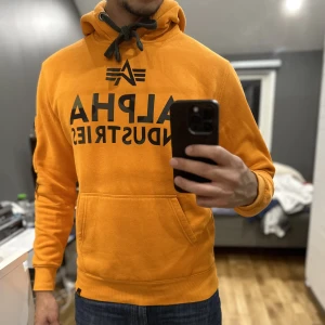 ALPHA INDUSTRIES HOODIE - Fräsch orange hoodie i helt okej med camouflage mönster på insidan. Endast slitning på där smörerna är. Någon månad gammal. Köpt från zalando för 879 kr.