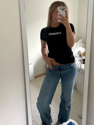 Svart t-shirt med STRONGER-tryck - Säljer en svart t-shirt med vit text där det står STRONGER på bröstet. T-shirten har korta ärmar och en klassisk rund halsringning. Passformen är normal och hade även kunnat passa en 38 