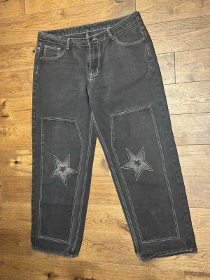 Svarta jeans med stjärnor och text - Unika svarta jeans med raka ben och kontrastsömmar. På framsidan finns broderade stjärnor på båda benen och på baksidan står det 'Nice weekend' i stor vit text. Jeansen har klassisk femficksmodell och är tillverkade i denim.