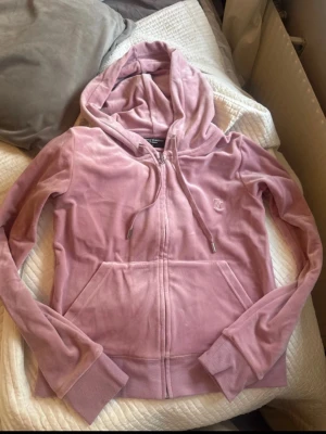 Rosa velour juicy couture  - Mysigt loungewear-set i mjuk rosa velour med zip-hoodie och matchande byxor. Hoodien har dragsko och fickor, byxorna har bred resår i midjan och fickor fram. Perfekt för chill dagar hemma eller när du vill vara extra bekväm.