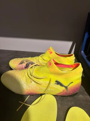 Gula Puma fotbollsskor med snörning - Säljer ett par riktigt snygga fotbollsskor från Puma i neon-gult med svarta loggor och inslag av rosa. Skorna har en strumpliknande passform, snörning och låg vikt för bästa känsla på planen. Perfekta för dig som vill sticka ut och ha bra grepp på konstgräs. 