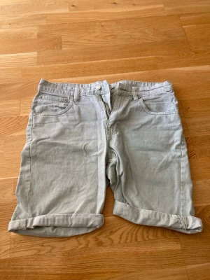 Ljus mintgröna  midwaist shorts med uppvik - Säljer ett par ljus mintgröna  shorts i bomull med klassisk femficksmodell och uppvikta benslut. Shortsen har bälteshällor och stängs med knapp och dragkedja. Perfekta för varma dagar och enkel att matcha med olika stilar.