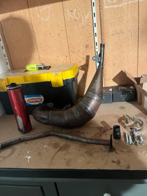 Avgassystem och delar till crossmoped - Säljer ett avgassystem till crossmoped med expansionkammare, röd ljuddämpare, fästen, fjädrar och rör. Metallkonstruktion med svetsade fogar och rå finish. Perfekt för dig som vill bygga eller uppgradera din moped.