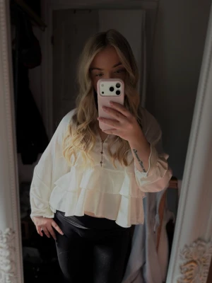 Vit volangblus med knappar - Säljer en söt vit blus med volanger och dekorativa knappar framtill. Blusen har lång ärm och v-ringning, samt ett lätt och luftigt tyg som ger en flowy känsla. Perfekt att styla med jeans eller kjol för en trendig look.