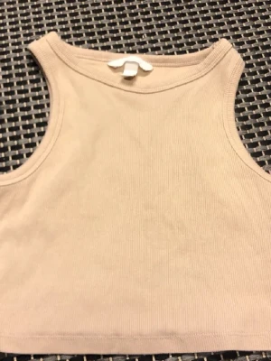 Beige ribbad linnetopp från H&M - Säljer en beige ribbad linnetopp från H&M i storlek S. Toppen är ärmlös och har en enkel, croppad passform som passar perfekt till jeans eller kjol. Materialet är mjukt och stretchigt, vilket gör den superbekväm att bära.