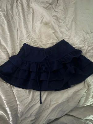 Mörkblå minikjol - Supersöt mörkblå kortkjol med flera volanglager. Den är köpt på Gina nån gång förra året men har bara använts ett få tal gånger. 