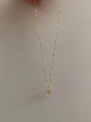 Guldhalsband med korshänge - Snyggt halsband i guld rostfritt med ett litet korshänge dekorerat med små glittrande stenar. Kedjan är tunn och elegant, perfekt för att ge en subtil touch till din outfit. Hänget har en klassisk form och gnistrar fint i ljuset.