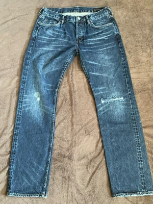 Allsaints jeans sellvedge  - Säljer ett par blå jeans från allsints med slitningar på både fram och baksida. Det är ett par sellvedge jeans vilket man ser på bild 3 och jeansen har även en snygg pläd som man ser på bild 4. Jeansen är endast använda cirka 5 gånger och är i ett riktigt bra skick. Bara att höra av sig vid minsta fundering och fråga. 🤗