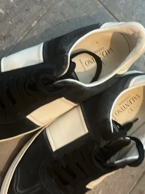 Svarta och vita sneakers från Valentino - Snygga sneakers från Valentino i svart och vitt läder. Klassisk låg modell med svarta skosnören och vit sula. Stilsäker design med kontrasterande färgblock och diskret logga på insidan. Perfekta för dig som gillar exklusiva märken och tidlös stil.