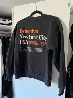 Mörkgrå sweatshirt med tryck från Gina Tricot - Mörkgrå sweatshirt med tryck på både fram- och baksida i vitt & orange. Perfekt streetwear.