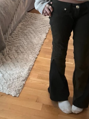 Svarta utsvängda jeans från True Religion - Säljer ett par svarta jeans från True Religion med utsvängda ben och hög midja. Jeansen har klassiska fickor fram och bak med dekorativa sömmar och silverfärgade knappar. Materialet är kraftigt denim som sitter snyggt och ger en cool siluett.