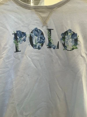 Ljusblå Ralph lauren sweatshirt - Super snygg ljusblå sweatshirt från polo Ralph lauren. Svart text och blommar på där texten säger ”polo” säljer då den är för liten. Storlek L fast i barnstorlekar, passar xxs. Ser lite gul ut på bilderna men den är inte det i verkligheten. Pris kan diskuteras och skriv vid frågor! ❣️