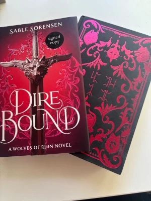 Dire Bound av Sable Sorensen - Säljer signerad special utgåva av boken 'Dire Bound' av Sable Sorensen. Den har en tvåsidig dustcover med illustration på ena sidan och standard omslag på andra sidan. Själva boken är dekorerad med ett rött skimrande mönster och utsidan av sidorna är illustrerade. Den har två varianter av kartan i boken och högkvalités sidor. Tveka inte att fråga eller be om fler bilder om ni är intresserade! 