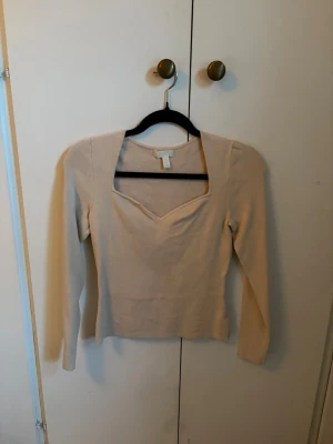 Beige långärmad topp - Trendig beige topp med lång ärm och snygg v-ringad hals. Figurnära passform och tjockt material. Ganska stor i passform.