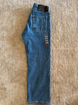 Levi's blå raka jeans 31x32 OANVÄNDA HELT NYA - Klassiska blå jeans från Levi's i rak modell. Jeansen har en bakficka med den ikoniska Levi's-sömmen och patch bak i midjan. Tillverkade i slitstark denim med tidlös look, perfekta till en avslappnad stil.