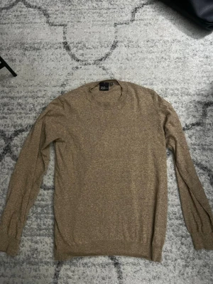 Beige stickad tröja Oscar Jacobson - Snygg beige stickad tröja från Oscar Jacobson. Tröjan har rund halsringning, långa ärmar och ribbade muddar vid ärmslut och nederkant. Tillverkad i Italien, mjukt material som känns lyxigt och passar perfekt till många olika stilar.