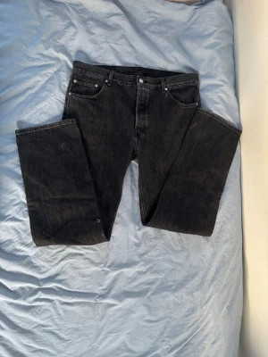 Svarta raka jeans från Weekday W-32 L-34 - Säljer ett par svarta jeans från Weekday med klassisk femficksdesign och raka ben. Jeansen har silverfärgade nitar och knapp. Tillverkade i denim med en snygg tvättad finish. Storlek W-32 L-34