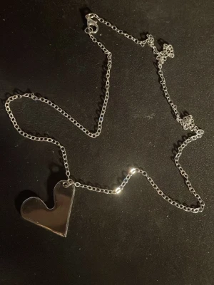 Silverfärgat halsband med hjärthänge - Snyggt halsband i silverfärg med en unik, asymmetrisk hjärtformad berlock. Kedjan är tunn och stilren, vilket gör att hjärtat verkligen står ut. Perfekt accessoar för dig som gillar minimalistisk och modern design.OBS! Materialet är okänt, kan ej garantera att det är rostfritt.