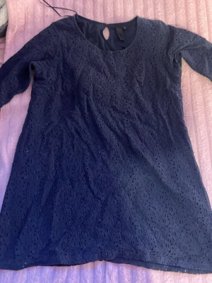 Mörkblå spetsblus med trekvartsärm - Snygg mörkblå blus i spets med rund halsringning och dekorativ knapp i nacken. Blusen har trekvartsärmar och ett lätt utställd passform. Perfekt att styla med jeans eller kjol för en trendig look.