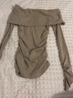 Beige offshoulder topp - Trendig beige offshoulder topp med långa ärmar och bred krage. Tunn och mjuk i materialet, perfekt för dig som gillar en stilren och enkel look. Snygg att matcha med både jeans och kjol.