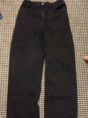 Svarta raka jeans från Lindex - Säljer ett par svarta jeans från Lindex i rak modell. Jeansen har klassisk femficksdesign och knappgylf. Perfekta till vardags för en avslappnad och stilren look. Materialet är mjukt och bekvämt, passar dig som gillar enkel och tidlös stil.