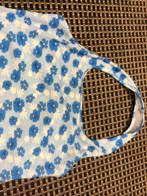 Blommig blå och vit linnetopp - Söt linnetopp med blåa blommor på vit botten. Toppen har ärmlös design med breda axelband och rundad halsringning. Perfekt för varma dagar och ger en fräsch sommarkänsla. Materialet känns lätt och luftigt.