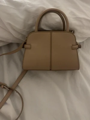 Beige minihandväska med axelrem - Snygg beige minihandväska i slätt konstläder med både handtag och justerbar axelrem. Väskan har en stilren, boxig form och minimalistisk design utan synliga loggor. Perfekt för dig som gillar en clean och modern look.
