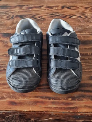 Svarta sneakers - Välanvända men håller en säsong till eller två. Det finns skav på högerskons överkant och sulorna är mer slitna på hälen än under övriga skon och kardborrarna fastnar inte jättebra men det går kanske att lösa för den som vill, kanske räcker att klippa ner den mjuka delen? Stl 31