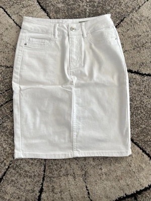 Vit jeanskjol från Calvin Klein  - Snygg vit jeanskjol i klassisk modell med fem fickor, bälteshällor och knappstängning fram. Kjolen har en rak passform och är tillverkad i ett stadigt bomullstyg. Perfekt att styla med en crop top eller hoodie för en chill look. 