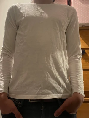 Vit långärmad basic tröja - En enkel och stilren vit långärmad tröja i mjukt material. Tröjan har rund halsringning och rak passform, perfekt att matcha med jeans eller under en skjorta. Inga synliga tryck eller loggor. Storlek 170 men mer som XS