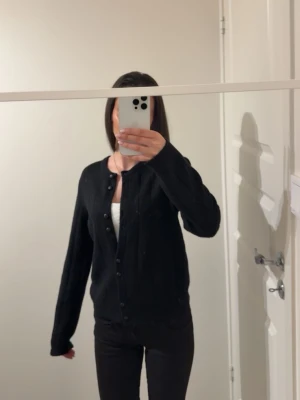 Svart kofta - En enkel svart kofta med rund halsringning och knäppning framtill. Koftan har långa ärmar och en rak passform, perfekt att slänga över en topp. Materialet ser mjukt och bekvämt ut, passar till det mesta i garderoben. Från bikbok i storlek XS.