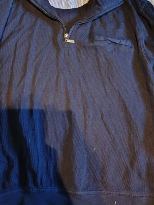 Marinblå half zip tröja från Clipper - Snygg marinblå tröja från Clipper med half zip och en bröstficka. Tillverkad i ett mjukt bomullstyg och har diskreta ränder i strukturen. Perfekt för dig som gillar klassisk och stilren design. Säljer då den är liten för mig