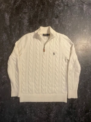 Vit kabelstickad tröja Polo Ralph Lauren - (Priset går att diskuteras) Den är Slimfit.  Kabelstickad vit tröja från Polo Ralph Lauren med  halv dragkedja och broderad marinblå logga på bröstet. 