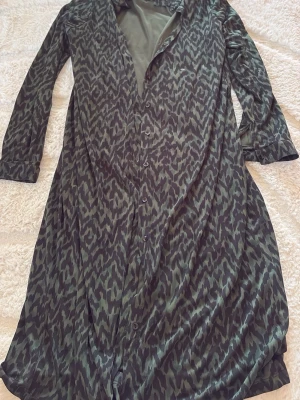 Mörkgrön långklänning från WE - Snygg långklänning från WE i mörkgrönt med zebramönster. Klänningen har knappar framtill och långa ärmar. Tillverkad i ett mjukt, lätt material som ger ett avslappnat men ändå stilrent intryck.