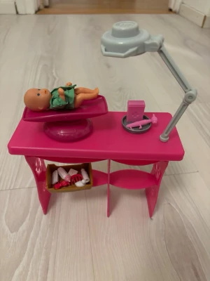 Barbie doktorlekset med dockor och tillbehör - Säljer ett Barbie doktorlekset med en Barbie-docka i vit rock, två små babydockor, rosa undersökningsbord, lampa och flera tillbehör som stetoskop, nappflaska, väska och medicinska accessoarer, där är 22 tillbehör. Allt i plast och i färgerna rosa, vitt och grått. Perfekt för dig som gillar att leka doktor och ta hand om dockor.                     Nypris:350kr