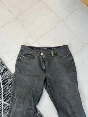 Grå jeans med nitar och detaljer - Snygga grå jeans från Jeane Blush med raka ben och coola nitar på fram- och bakfickor. Jeansen har klassisk femficksmodell och dekorativa detaljer på bakfickorna. Perfekta för dig som gillar en edgy stil.