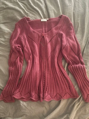 Rosa stickad cardigan från Cappuccini - Säljer en rosa stickad cardigan från Cappuccini i storlek M. Koftan har långa ärmar, dekorativa hålmönster och knäppning med en knapp framtill. Materialet är mjukt och stretchigt, perfekt för lager på lager och en snygg detalj till din outfit.